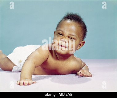 1960 AFRICAN-AMERICAN BABY BOY WEARING COUCHE AVEC UN CLIN D'UN OEIL FERMÉ Banque D'Images