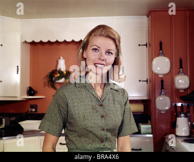 1960 PORTRAIT YOUNG BLONDE WOMAN IN KITCHEN SMILING RETRO Banque D'Images