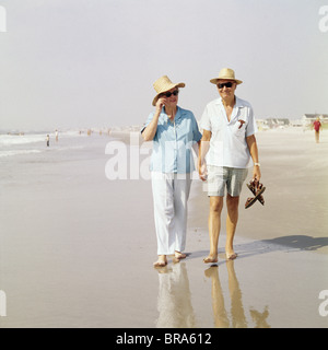 1980 1980 RETRO COUPLE WALKING BEACH HOLDING HANDS portant des chapeaux de paille Banque D'Images