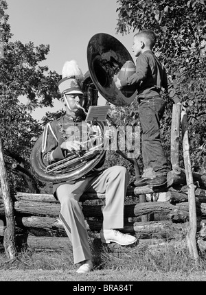 1950 TEEN JOUANT UN TUBA ASSIS CLÔTURE DANS UN UNIFORME DE BANDE BOY STANDING ON FENCE HOLDING FOOTBALL WATCHES Banque D'Images