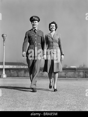 1940 SMILING COUPLE en train de marcher de l'AVANT L'HOMME EN UNIFORME Banque D'Images