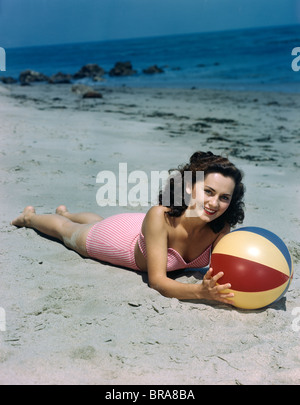 Années 1940 Années 1950 BRUNETTE WOMAN LYING ON BEACH HOLDING BEACH BALL Banque D'Images