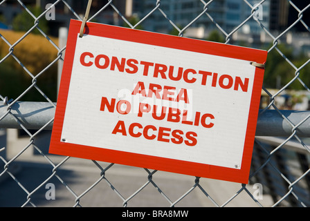 Panneau d'avertissement rouge et blanc "Zone de construction - Accès interdit au public" accroché à une clôture en grillage dans un environnement urbain. Banque D'Images