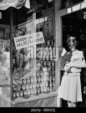 1940 FEMME TRANSPORTANT DES COLIS DANS LA PORTE DE LA VILLE DE NEW YORK DELICATESSEN AFFICHANT UN PANNEAU SANDWICH DE SORTIR NE SONT PAS RATIONNÉS Banque D'Images