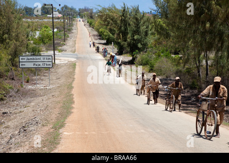 Makunduchi, Zanzibar, Tanzanie. Les cyclistes et les femmes transportant des charges marcher jusqu'à la colline à l'extérieur de la ville. Banque D'Images