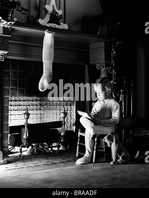 1940 Petite fille assise à côté d'une cheminée AVEC UN BAS DE NOËL À ÉCRIRE UNE LETTRE Banque D'Images