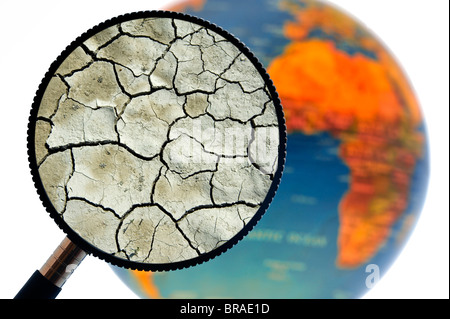 La terre craquelée par la sécheresse vu à travers une loupe tenu contre allumé globe terrestre Banque D'Images