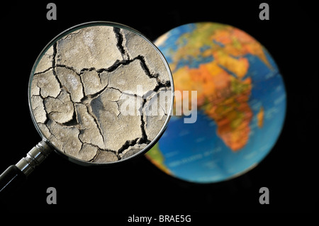 La terre craquelée par la sécheresse vu à travers une loupe tenu contre allumé globe terrestre Banque D'Images