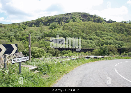 Panneau routier disant Millers Dale, Derbyshire Peak District National Park, Angleterre, Royaume-Uni, avec le viaduc de chemin de fer désaffectée dans l'arrière-plan Banque D'Images