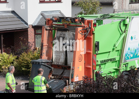 La collecte des déchets ménagers Bin men loading wheelie bins sur camion dans la rue. Anglesey au nord du Pays de Galles, Royaume-Uni, Angleterre. Banque D'Images