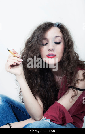 Les jeunes aux cheveux longs bouclés belle brunette woman with cigarette isolé sur fond blanc Banque D'Images