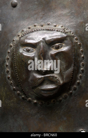 Un bouclier en bronze celtique t> Europe centrale, 4ème - 2ème siècle C.-B., Bronze avec patine brunâtre-verte. Ovale pointu, blindage légèrement bombé en bronze épais. Au centre, un bossage riveté avec un motif visage en relief. Le périmètre porte une bordure décorative en relief. Un bord légèrement tourné sous la jante et une perforation circonférentielle fine pour la garniture, certains trous portent les rivets en bronze restants. De chaque côté du bossage, quatre grands rivets pour la poignée, un rivet déchiré. Recherche archéologique nettoyée. Hauteur 59 cm. Blindage en bronze celtique extrêmement rare. Boucliers en elle, Banque D'Images