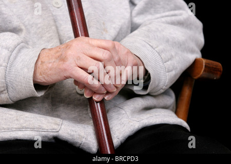 Une femme âgée's hands holding sa canne sur ses genoux Banque D'Images