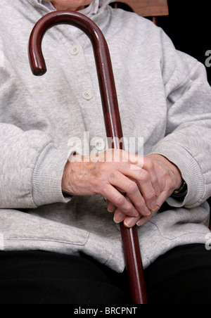 Une femme âgée's hands holding sa canne sur ses genoux Banque D'Images