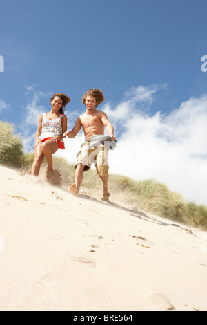Jeune couple fonctionnant en bas sur la plage de dunes de sable Banque D'Images