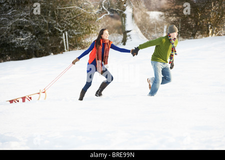 Woman Pulling Sled à travers champ neigeux Banque D'Images