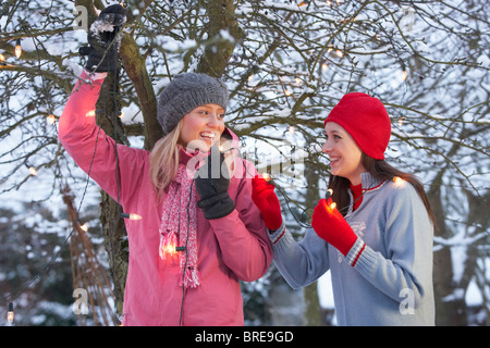 Deux adolescentes pendaison Fairy Lights in Tree avec les glaçons en premier plan Banque D'Images