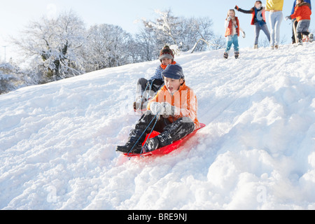 Jeune garçon de la luge en bas de la colline avec l'observation de la famille Banque D'Images