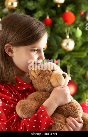 Jeune Fille de câliner Ours in front of Christmas Tree Banque D'Images