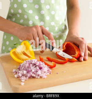 Woman slicing poivre rouge à côté de l'oignon rouge en dés et la moitié de poivron jaune Banque D'Images