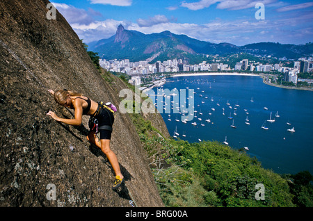 Une femme rock remonte le côté de la Montagne du Pain de Sucre à Rio de Janeiro avec un fond de Botafogo bay et le Corcovado. Banque D'Images