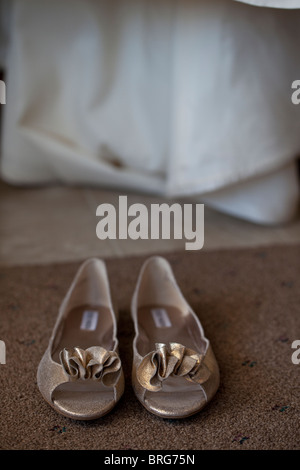 Paire de chaussures de couleur bronze avec des volants avec le bord inférieur de la robe de mariée dans l'arrière-plan. Banque D'Images