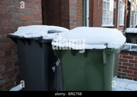 Noir et vert à l'extérieur d'un wheelie bins maison mitoyenne en briques recouvert de neige en attente d'être recueillis et vidé par le bin men Banque D'Images