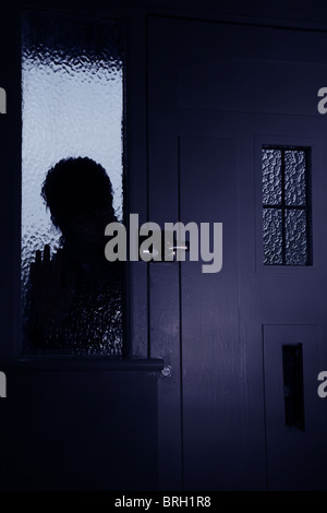 Silhouette homme intrus regardant à travers une fenêtre opaque à côté d'une porte d'entrée Banque D'Images