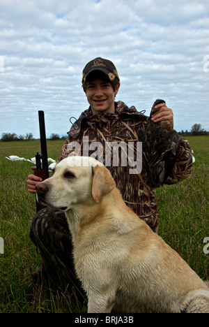 Jeune chasseur de canard portant des vêtements de camouflage holding dead American widgeon et fusil dans l'orge récoltée champ de chaumes Banque D'Images