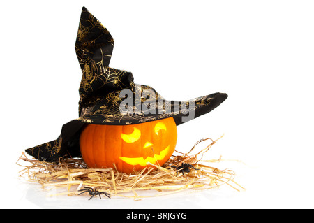 Jack o lantern Halloween citrouille sculptée portant chapeau de sorcière sur la paille avec des araignées et fond blanc Banque D'Images