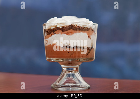 Un solo basse grosse mousse au chocolat avec crème fouettée assis dans un bol en verre sur un fond bleu Banque D'Images