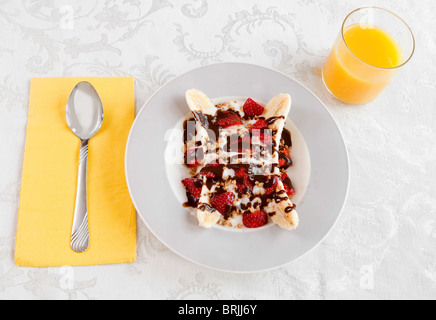 Un bol de petit-déjeuner sain banana split avec yaourt et pas de calories sur fondant au chocolat blanc un bol avec du jus d'orange Banque D'Images