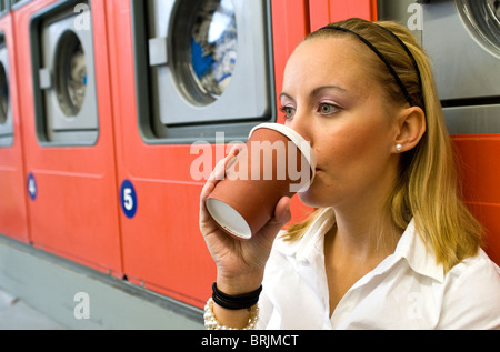 Woman Drinking Coffee in Laundromat Banque D'Images