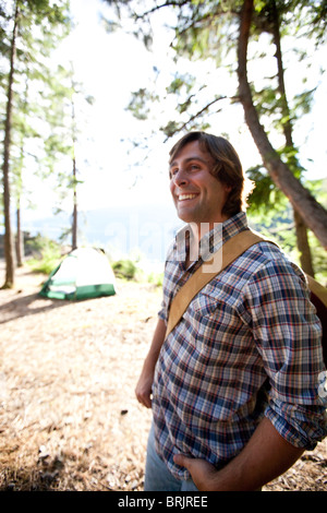 Un jeune adulte avec une guitare sur son épaule donne avec tente dans l'arrière-plan sur une journée ensoleillée dans l'Idaho. Banque D'Images