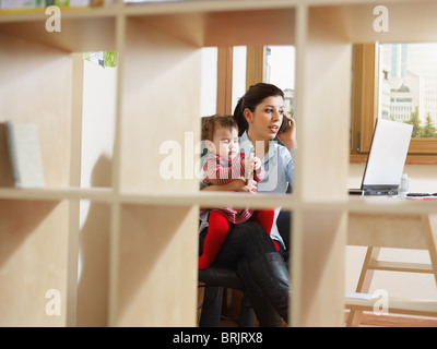 Le multitâche businesswoman holding son bébé et talking on mobile phone Banque D'Images