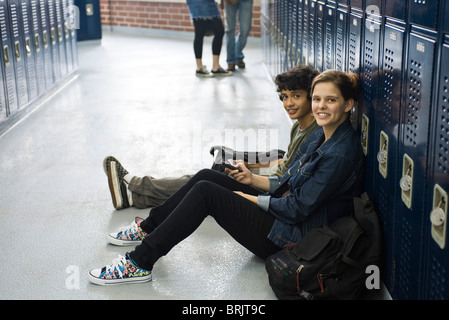 High school student sitting on floor with friend par casiers dans le couloir de l'école Banque D'Images