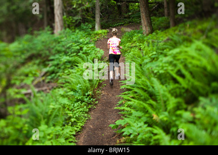 Jeune femme trail running à travers un champ de fougères luxuriantes. Banque D'Images