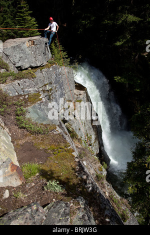 Un jeune homme vers le bas d'une falaise rappels à côté d'une chute dans l'Idaho. Banque D'Images