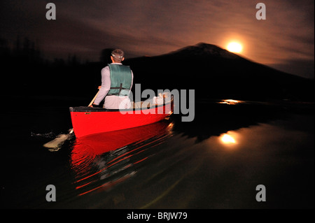 Un homme canoë dans un bateau rouge dans la nuit sur un lac de montagne dans l'Oregon. Banque D'Images