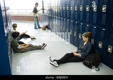 High school students sitting on floor casiers par l'utilisation de téléphones cellulaires Banque D'Images