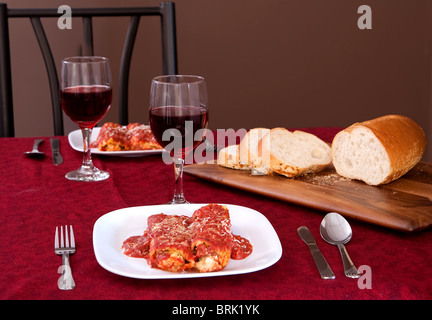 Deux plaques de manicotti farcis, un pain de tranches de pain italien et 2 verres de vin Banque D'Images