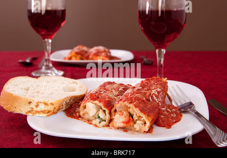 Deux plaques de manicotti farcis, un pain de tranches de pain italien et 2 verres de vin Banque D'Images