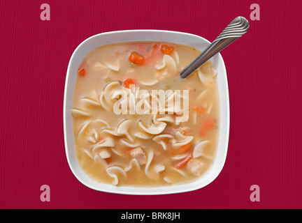 Un grand bol de soupe au poulet et nouilles dans un bol blanc sur une nappe rouge fond. vue d'en haut. Banque D'Images