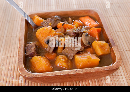 Bol de ragoût de boeuf maison avec des carottes et des patates douces dans un bol en bois sur napperon Banque D'Images