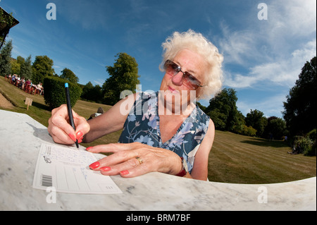 Vieille Femme assis à l'extérieur écrit une carte postale sur une chaude journée d'été. Banque D'Images