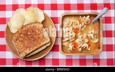 Un sandwich au fromage avec du chips et un bol de soupe au poulet et nouilles maison traditionnelle. la nourriture sur des plats rustiques Banque D'Images