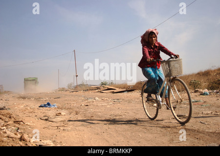 Chasse une femme vivant dans la pauvreté ses promenades en vélo sur un chemin de terre à la décharge de Stung Meanchey à Phnom Penh, Cambodge. Banque D'Images