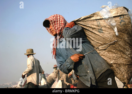 Un travailleur utilise une gaffe pour stabiliser un sac rempli de déchets à la décharge de Stung Meanchey à Phnom Penh, Cambodge. Banque D'Images