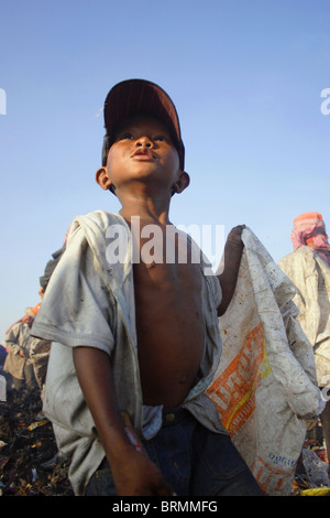 Un enfant travailleur transporte un sac à déchets lors de la recherche dans les ordures à la décharge de Stung Meanchey à Phnom Penh, Cambodge. Banque D'Images