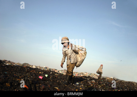 Un enfant travailleur transporte un sac à déchets lors de la recherche dans les ordures à la décharge de Stung Meanchey à Phnom Penh, Cambodge. Banque D'Images